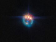 Una piccola immagine di una galassia distorta dalla lente gravitazionale in un anello fioco. Nella parte superiore dell'anello ci sono tre punti molto luminosi con punte di diffrazione che fuoriescono da essi, uno accanto all'altro: in realtà si tratta di copie di un singolo quasar nella galassia, duplicate dalla lente gravitazionale. Al centro dell'anello, la galassia ellittica che esegue la lente appare come un piccolo punto blu.